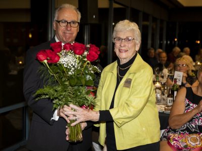Executive Board member and Master of Ceremonies Gary Bras presents flowers of apprecation to Volunteer and Executive Board member Joanne Bilbo.